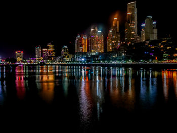 Illuminated buildings by river against sky at night