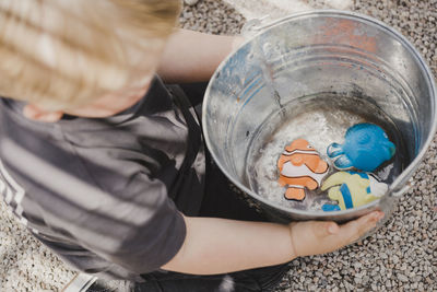 From above of unrecognizable child playing with plastic toy fish in water in bucket
