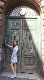 Portrait of young woman standing against door of building
