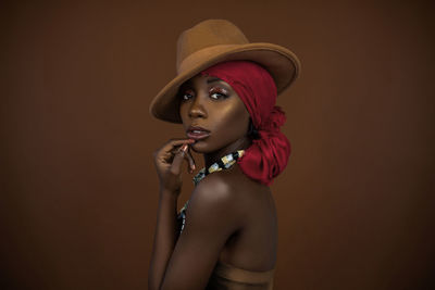 Portrait of beautiful young woman wearing hat against brown background
