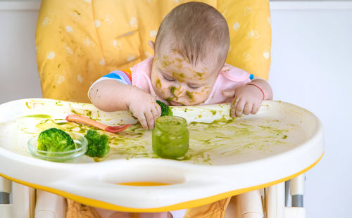 Messy cute baby girl playing with food at home