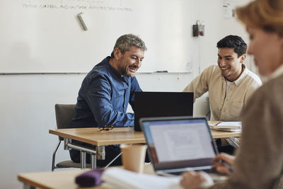 Smiling teacher and student looking at laptop while sitting in classroom