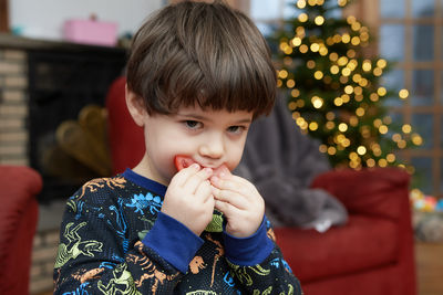 Expressive young boy is eating a tomato in front of a christmas tree in the living room