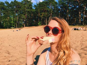 Beautiful woman having ice cream sandwich at beach against trees