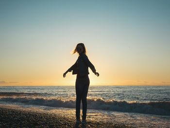 Woman standing on shore at beach against sky during sunset