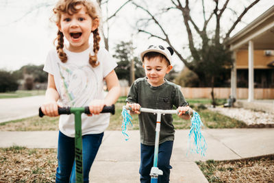 Young sister and brother riding scooters outside in front yard