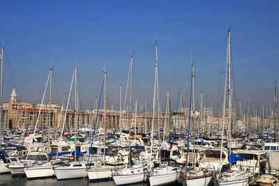 Sailboats moored in harbor against clear blue sky