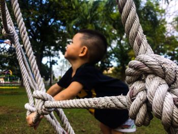 Side view of boy holding rope while playing in park