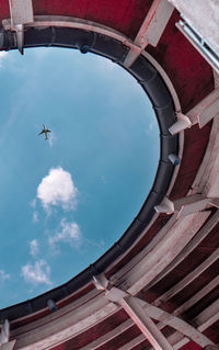 Low angle view of airplane flying seen through built structure against sky