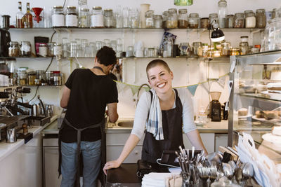 Young happy female owner at cafe with male colleague working in background