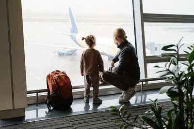 Man with girl ready to fly by airplane and the airport. father and child looking though the lounge