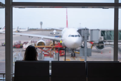 Woman sitting on her back, looks through the airport window, waiting for her flight.