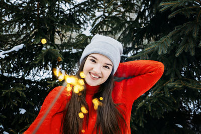 Outdoor portrait of happy cute latina girl in winter hat and red sweater posing with sparkler