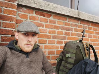 Portrait of man sitting by brick wall