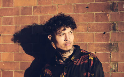 Portrait of young man standing against brick wall