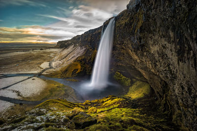 Scenic view of waterfall against cloudy sky