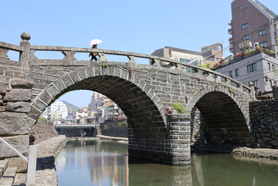 Arch bridge over river in city against clear sky