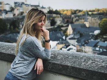 Young woman looking away while standing on retaining wall in city