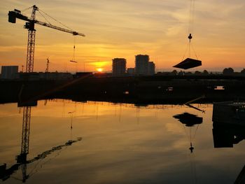 Silhouette cranes at construction site against sky during sunset