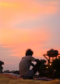 Rear view of man sitting against orange sky