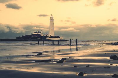 Lighthouse at beach against sky during sunset