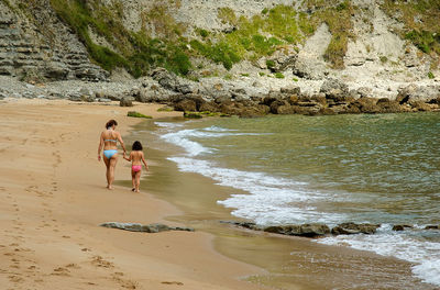 Rear view of mother and daughter walking on shore