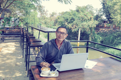 Portrait of mature man with laptop sitting at outdoor cafe