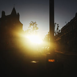 Silhouette buildings by street against sky during sunset