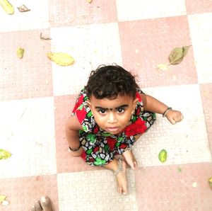 Portrait of cute baby girl sitting on tiled floor