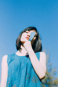 Portrait of young woman standing against blue sky