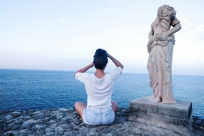 Rear view of women sitting by sea against sky