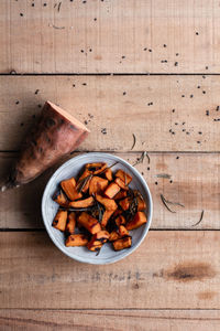 Top view of half of raw sweet potato and pieces of baked sweet potato in bowl on rustic wooden table