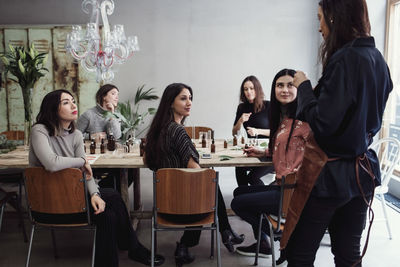 Multi-ethnic female colleagues looking at mid adult owner standing in perfume workshop