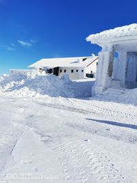 Snow covered house by building against sky