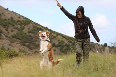 Woman with dog standing on field against sky