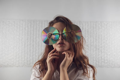 Portrait of young woman wearing compact disc against wall