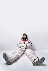 Serious young asian female in spacesuit looking at camera while sitting near gray wall during space mission