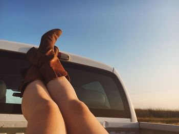 Low section of woman sitting on car against sky