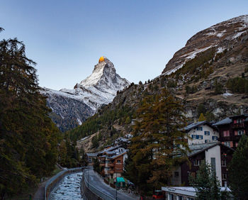 Road amidst buildings and mountains against clear sky