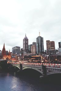 Bridge over river by buildings against sky in city