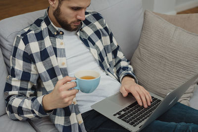 Midsection of man using laptop while sitting on sofa at home