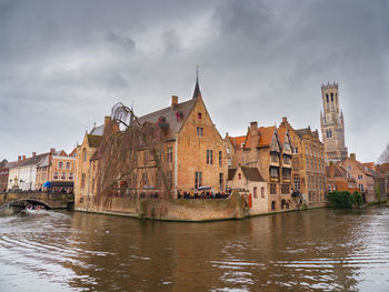 View of buildings by river against cloudy sky