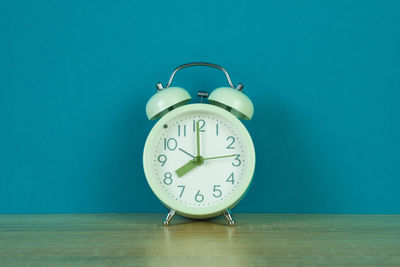 Close-up of clock on table against blue wall