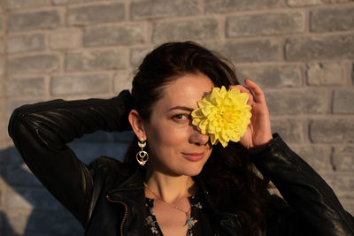 Portrait of smiling woman with yellow flower against wall