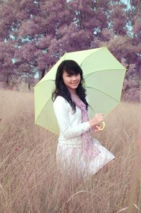 Young woman holding umbrella while standing on field