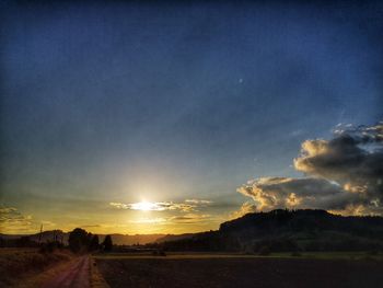Road amidst field against sky during sunset