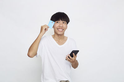 Portrait of smiling young man using smart phone against white background