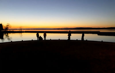 Silhouette people standing on lake against sky during sunset