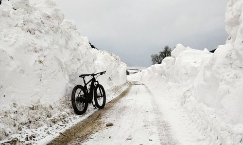 Bicycle parked on snow covered landscape against sky