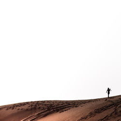 Man walking on desert against clear sky